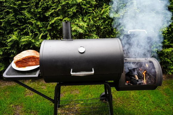 Ein schwarzer Smoker steht auf einer grünen Wiese.